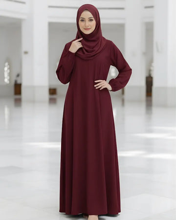 Woman wearing a burgundy Abaya and hijab in a white indoor setting