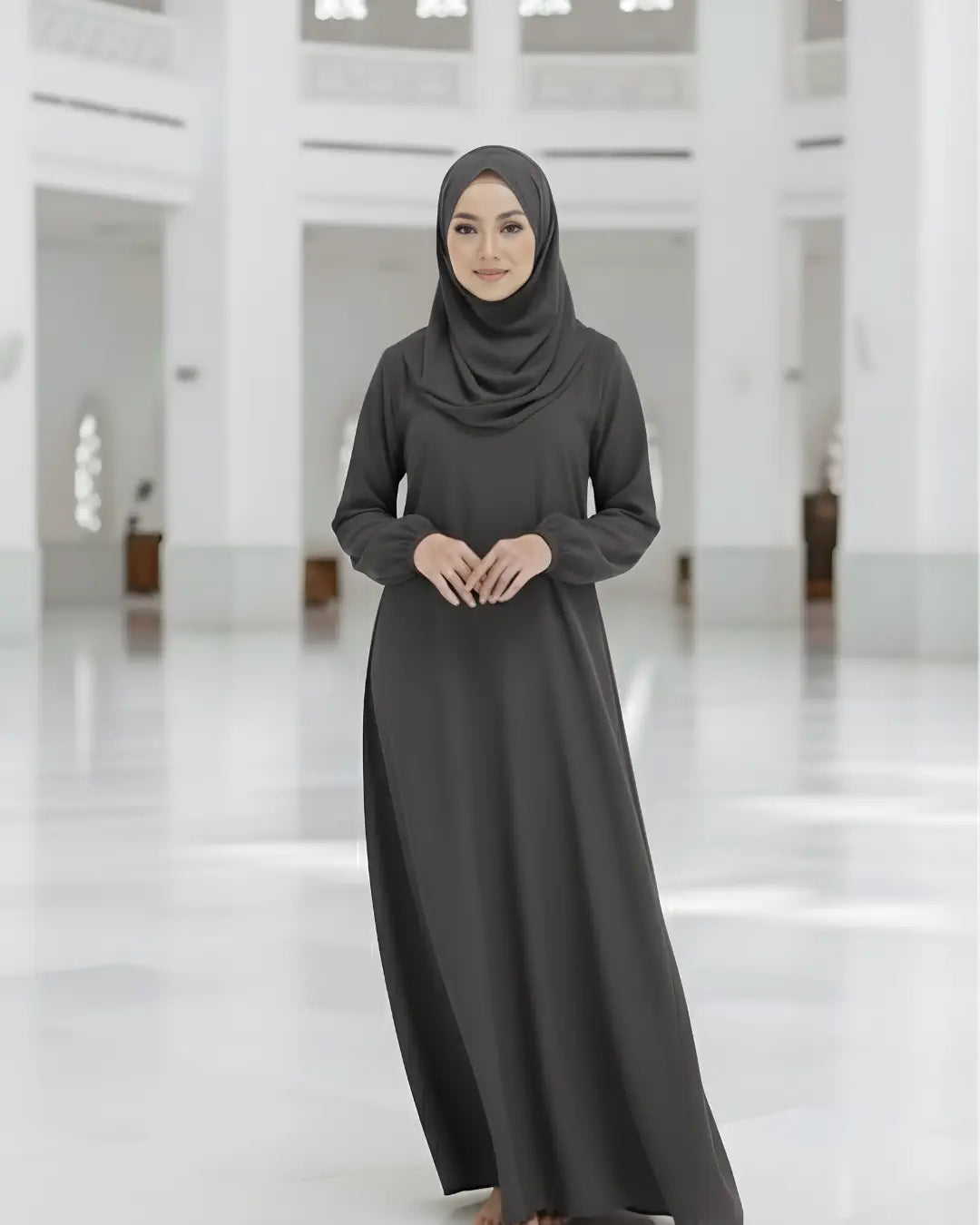 Woman wearing a long dark gray abaya and hijab in a bright, minimalistic indoor setting.