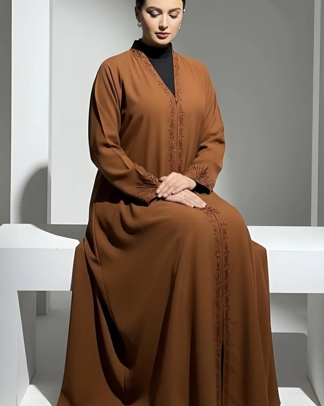 Woman wearing a brown ABAYA sitting on a white bench against a gray wall.