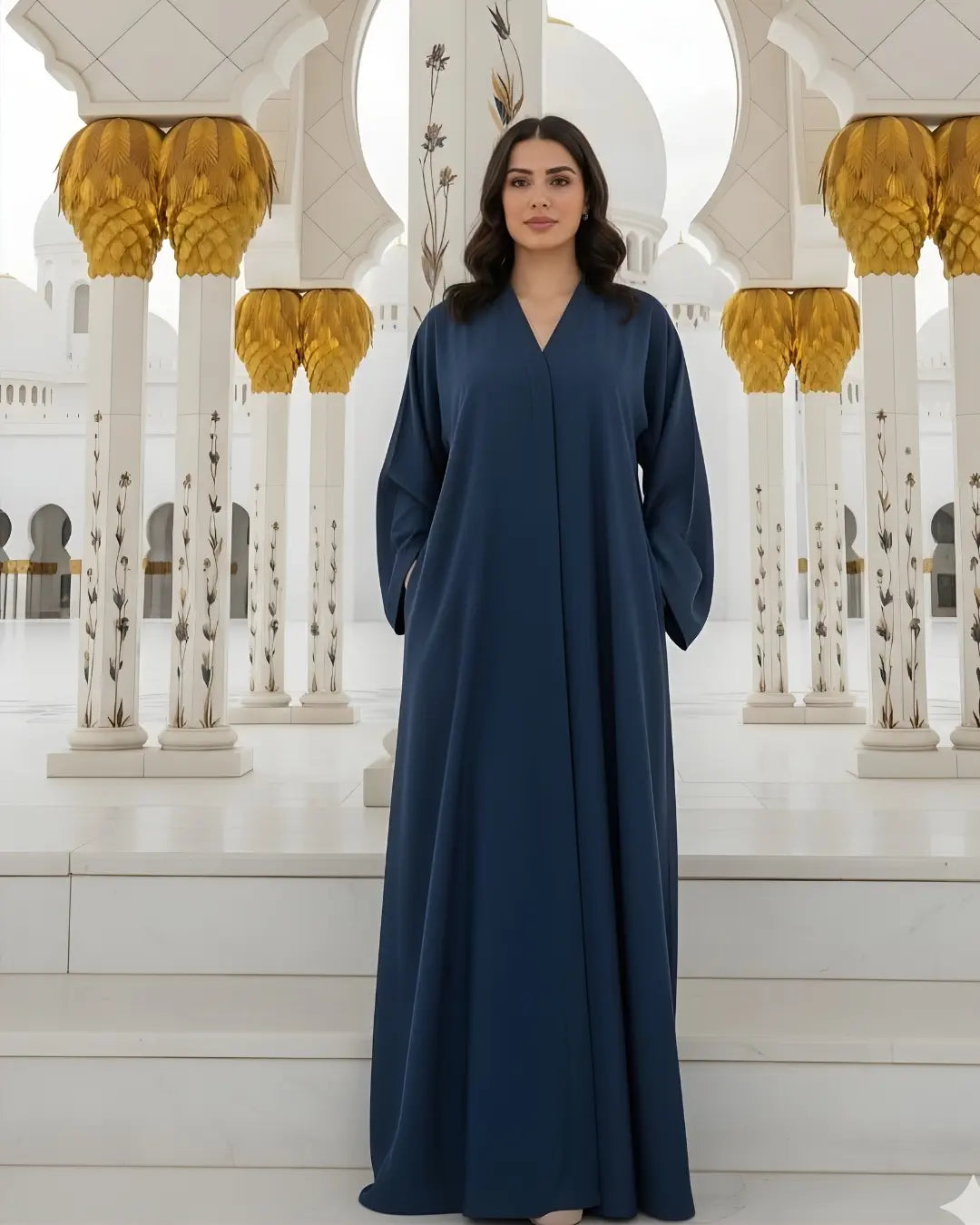 Woman in a long blue abaya standing in front of a white architectural background with gold accents.